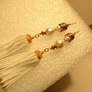 May include: A pair of white beaded tassel earrings with gold accents and a pearl drop on each earring.