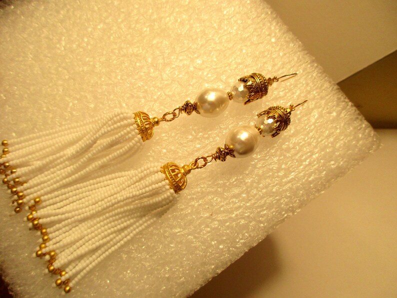 May include: A pair of white beaded tassel earrings with gold accents and a pearl drop on each earring.