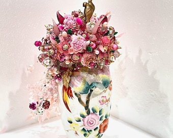 May include: A pink and white floral arrangement with birds and beads in a white porcelain vase with a floral design.