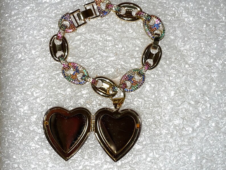 May include: A gold chain bracelet with a colorful, multi-faceted design. The bracelet has a heart-shaped locket attached to it.