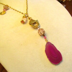 May include: A gold chain necklace with a pink agate pendant, pink and gold beads, and a gold charm.