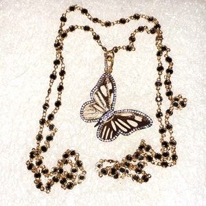May include: A gold chain necklace with black beads and a large butterfly pendant with clear and white stones.