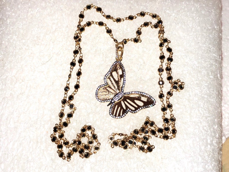 May include: A gold chain necklace with black beads and a large butterfly pendant with clear and white stones.