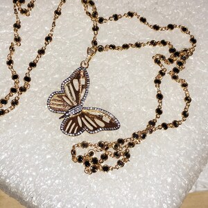 May include: A gold chain necklace with black beads and a gold butterfly pendant with clear stones.