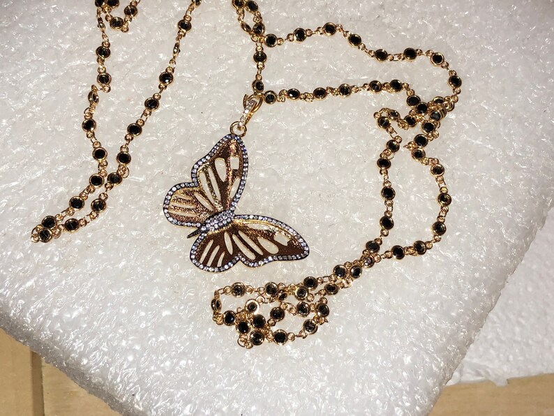 May include: A gold chain necklace with black beads and a gold butterfly pendant with clear stones.
