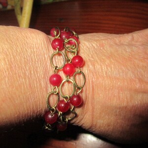 May include: A gold chain bracelet with red beads. The bracelet is layered with multiple strands of chain and beads.