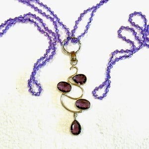 May include: A purple amethyst gemstone necklace with a pendant featuring a gold swirl design and multiple amethyst stones.