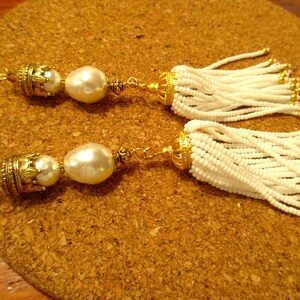 May include: A pair of white beaded tassel earrings with gold accents and a large white pearl on each earring.