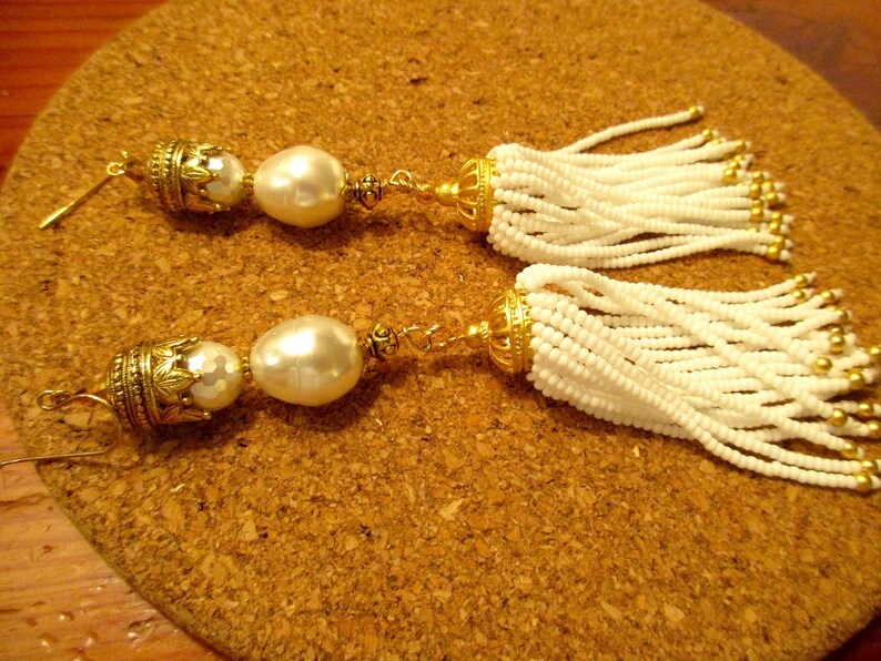 May include: A pair of white beaded tassel earrings with gold accents and a large white pearl on each earring.