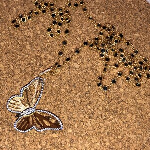 May include: A gold chain necklace with a butterfly pendant. The chain is made of small gold links with black beads. The butterfly pendant is detailed with gold and white accents.