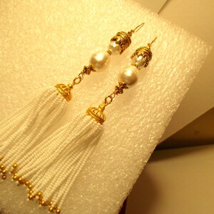 May include: A pair of gold tone earrings with white pearl beads and white beaded tassels.