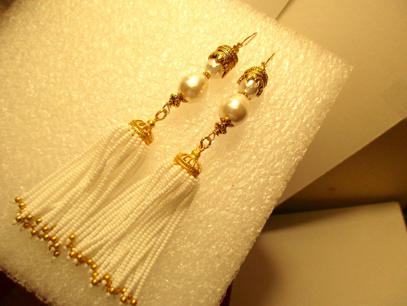 May include: A pair of gold tone earrings with white pearl beads and white beaded tassels.
