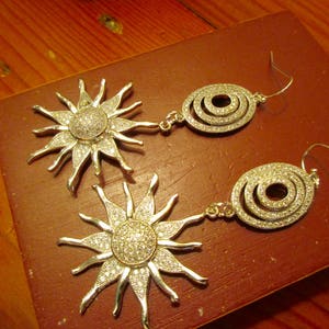 May include: Two pairs of silver earrings with a sunburst and circle design. The earrings are adorned with sparkling rhinestones.