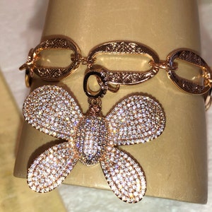 May include: A gold chain bracelet with a butterfly charm. The butterfly is covered in sparkling clear stones.