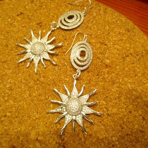 May include: A pair of silver earrings with a sunburst design and a circular design. The earrings are set with clear crystals.