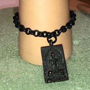 May include: Black chain bracelet with a gold-toned pendant featuring a detailed image of a seated Buddha.