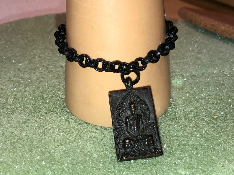 May include: Black chain bracelet with a gold-toned pendant featuring a detailed image of a seated Buddha.