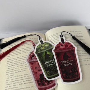 Könnte beinhalten: Drei Lesezeichen in Bubble-Tea-Form mit schwarzen Quasten. Eines ist grün mit "Horror Reads", ein anderes ist rot mit "Thriller reads", und das letzte ist rot mit "S Rom Re". Jedes hat eine Silhouette und Schädeldetails.