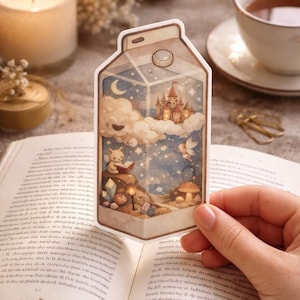 Könnte beinhalten: Ein skurriler Aufkleber in Form eines Milchkartons, der eine verträumte Illustration eines Schlosses, Wolken und einer Katze beim Lesen eines Buches zeigt. Der Aufkleber wird über einem offenen Buch gehalten.