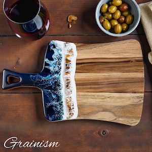 Könnte beinhalten: Holzservierbrett mit dunkelblauem Griff und weiß-blauem Harzdesign. Das Brett hat eine natürliche Holzmaserung. Das Wort "Grainism" ist unten aufgedruckt.