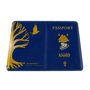 Puede incluir: Una funda de pasaporte azul marino con gráficos dorados. La funda presenta un diseño de árbol, un pájaro volando y la palabra "PASSPORT" en dorado. La palabra "ASGARD" también se muestra en dorado.