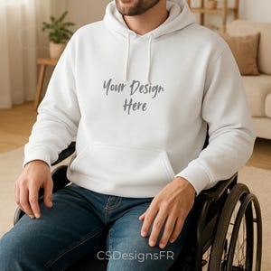May include: White hooded sweatshirt with a front pocket and drawstring. The text "Your Design Here" is printed on the front. The bottom of the image has the text "CSDesignsFR". The person is wearing blue jeans.