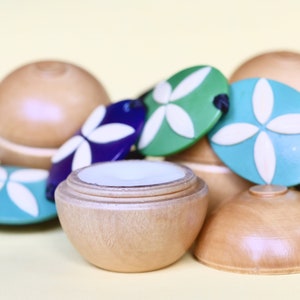 May include: A wooden container with a lid, featuring a white floral design on the lid. The container is surrounded by colorful wooden beads with white floral designs.