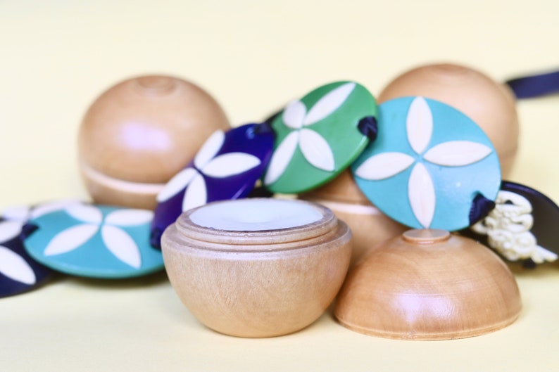 May include: A wooden container with a lid, featuring a white floral design on the lid. The container is surrounded by colorful wooden beads with white floral designs.