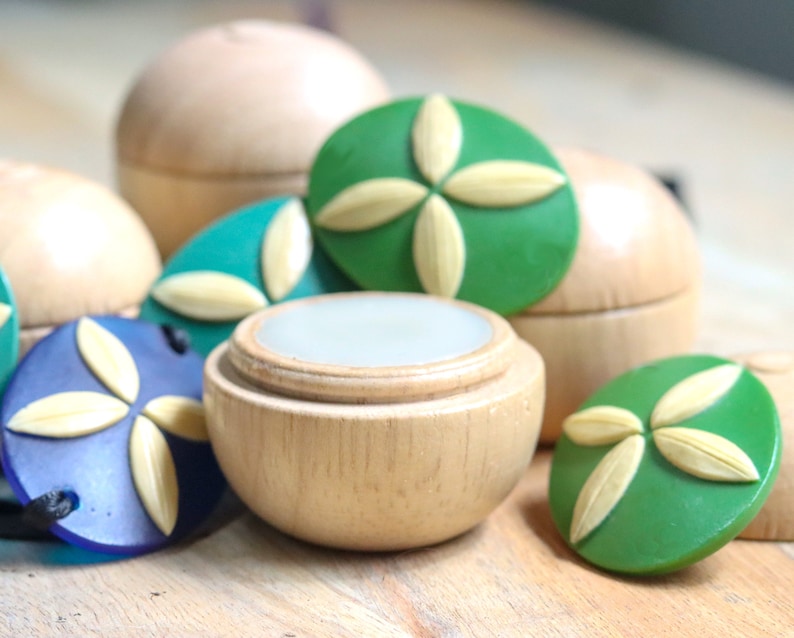May include: A set of wooden containers with lids, each featuring a different colored, decorative, floral design. The containers are ideal for storing small items like lip balm or jewelry.