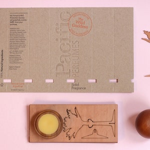 May include: A cardboard box with a brown background and white text. The text reads "100% New Zealand Made", "100% Sustainable", "100% Natural Ingredients", "Pacific Perfumes", "The Wild Goddess", "Solid Fragrance".