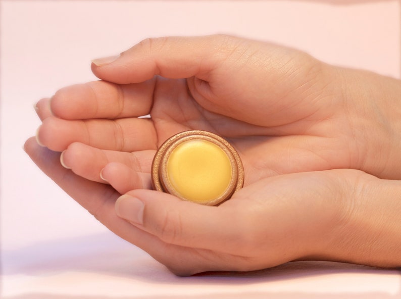 May include: A small round container of yellow balm in a wooden container with a gold rim.