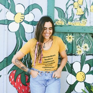 Flowy, soft mustard colored tshirt says "Peacemaker Healers Explorers Artists Visonaries Lovers" 
Printed with black ink. Perfect for any boho woman.