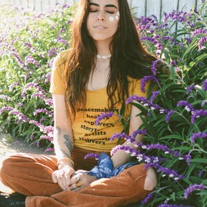 Flowy, soft mustard colored tshirt says "Peacemaker Healers Explorers Artists Visonaries Lovers" 
Printed with black ink. Perfect for any boho woman.