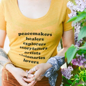 Flowy, soft mustard colored tshirt says "Peacemaker Healers Explorers Artists Visonaries Lovers" 
Printed with black ink. Perfect for any boho woman.