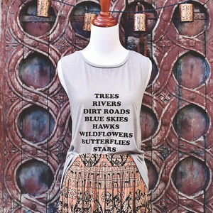 Light grey muscle tank.  Inspired by our love of Texas.  Says, Trees Rivers Dirt Roads Blue Skies Hawks Wildflowers Butterflies Stars on front int black ink.
