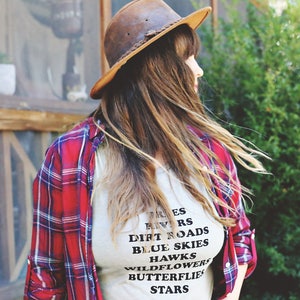 Light grey muscle tank.  Inspired by our love of Texas.  Says, Trees Rivers Dirt Roads Blue Skies Hawks Wildflowers Butterflies Stars on front int black ink.