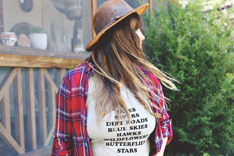 Light grey muscle tank.  Inspired by our love of Texas.  Says, Trees Rivers Dirt Roads Blue Skies Hawks Wildflowers Butterflies Stars on front int black ink.