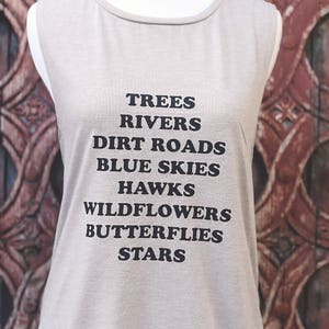 Light grey muscle tank.  Inspired by our love of Texas.  Says, Trees Rivers Dirt Roads Blue Skies Hawks Wildflowers Butterflies Stars on front int black ink.