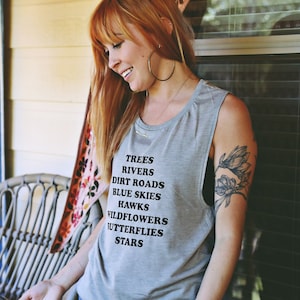Light grey muscle tank.  Inspired by our love of Texas.  Says, Trees Rivers Dirt Roads Blue Skies Hawks Wildflowers Butterflies Stars on front int black ink.