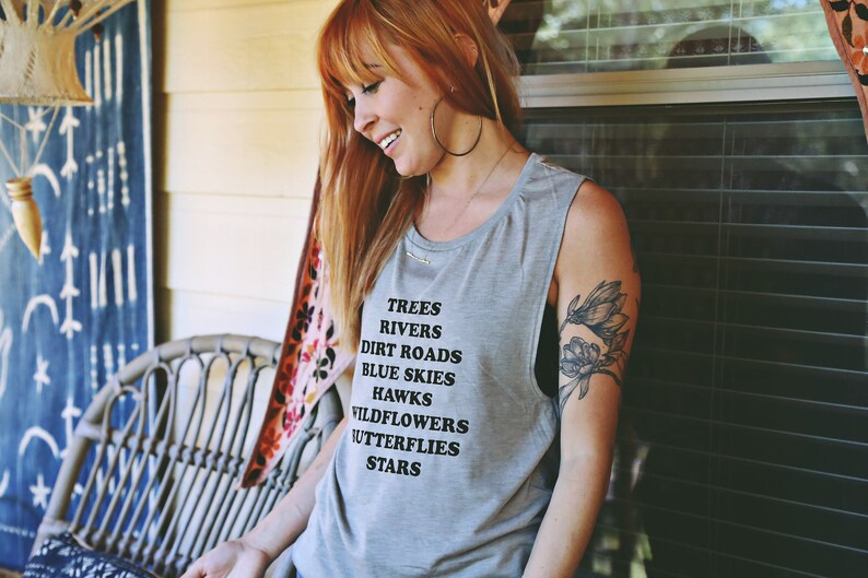 Light grey muscle tank.  Inspired by our love of Texas.  Says, Trees Rivers Dirt Roads Blue Skies Hawks Wildflowers Butterflies Stars on front int black ink.