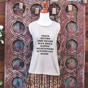 Light grey muscle tank.  Inspired by our love of Texas.  Says, Trees Rivers Dirt Roads Blue Skies Hawks Wildflowers Butterflies Stars on front int black ink.