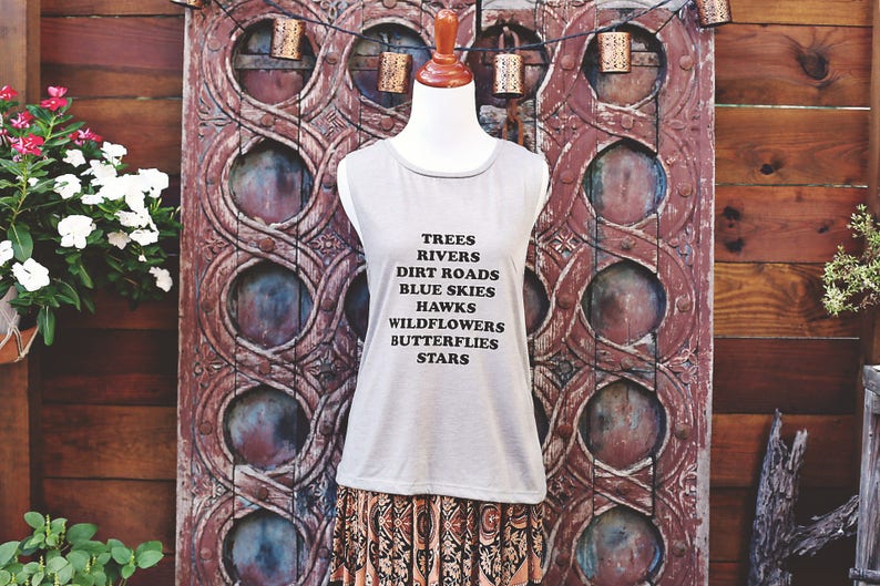 Light grey muscle tank.  Inspired by our love of Texas.  Says, Trees Rivers Dirt Roads Blue Skies Hawks Wildflowers Butterflies Stars on front int black ink.