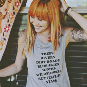 Light grey muscle tank.  Inspired by our love of Texas.  Says, Trees Rivers Dirt Roads Blue Skies Hawks Wildflowers Butterflies Stars on front int black ink.