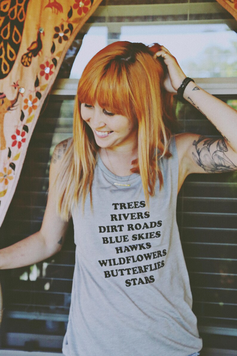 Light grey muscle tank.  Inspired by our love of Texas.  Says, Trees Rivers Dirt Roads Blue Skies Hawks Wildflowers Butterflies Stars on front int black ink.