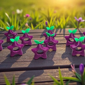 Puede incluir: Una colección de objetos morados en forma de estrella con detalles de hojas verdes, dispuestos sobre una superficie de madera. Los objetos tienen un agujero en el centro y están colocados sobre un fondo borroso de hierba y flores.