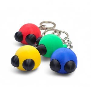 May include: Four colorful keychains in red, green, yellow, and blue. Each keychain features a spherical design with two black, cone-shaped accents, resembling eyes. The keychains are attached to silver metal key rings.