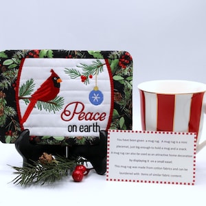 May include: A Christmas-themed mug rug with a red cardinal, pine branches, and the words "Peace on Earth." The mug rug is displayed with a red and white striped mug. A card provides information about the mug rug.