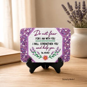 Può includere: Una targa rettangolare in tessuto trapuntato con bordo floreale viola e centro bianco. Il testo recita: Do not fear FOR I AM WITH YOU I WILL STRENGTHEN YOU and help you. Is. 41:10. È esposta su un supporto in plastica nera.