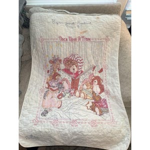 May include: A cream-colored quilted baby blanket featuring an embroidered scene of teddy bears reading a book. The text "Once Upon A Time" is stitched in pink above the bears, with "Byron Joseph Headrick 9-4-97" embroidered at the top.