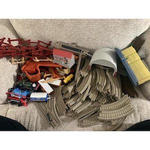 May include: A collection of toy train set pieces, including tracks, bridges, a tunnel, and miniature trains. The set features a variety of colors, including red, blue, green, and tan. The tracks are curved and straight, and the set includes a small building.